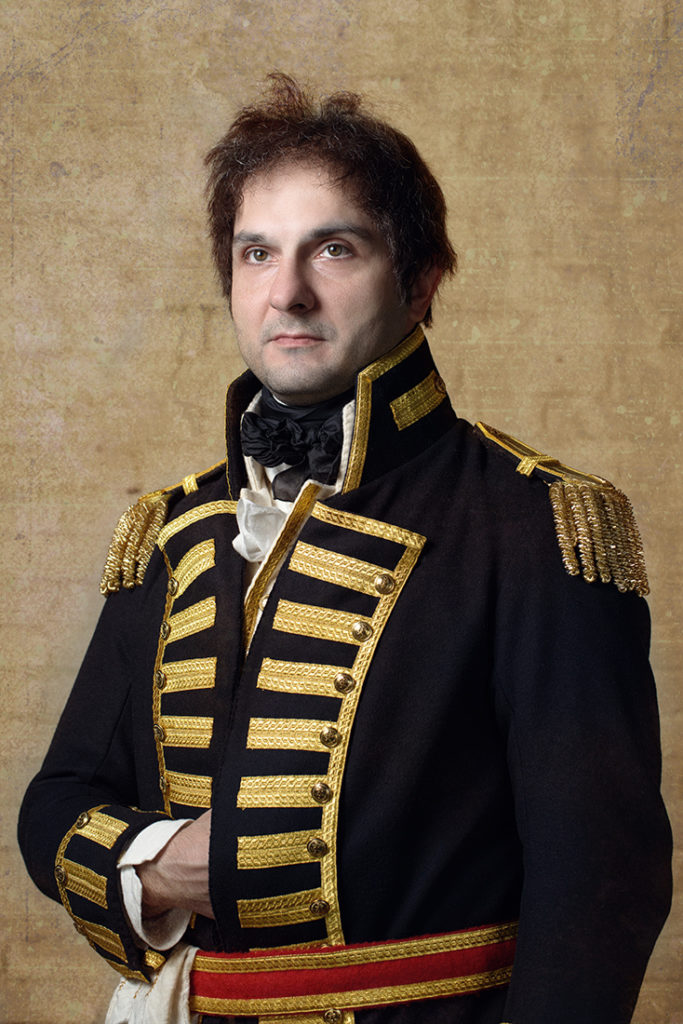 a man wearing a custom regency wig, dark hair in a short style with a regency era military uniform.
