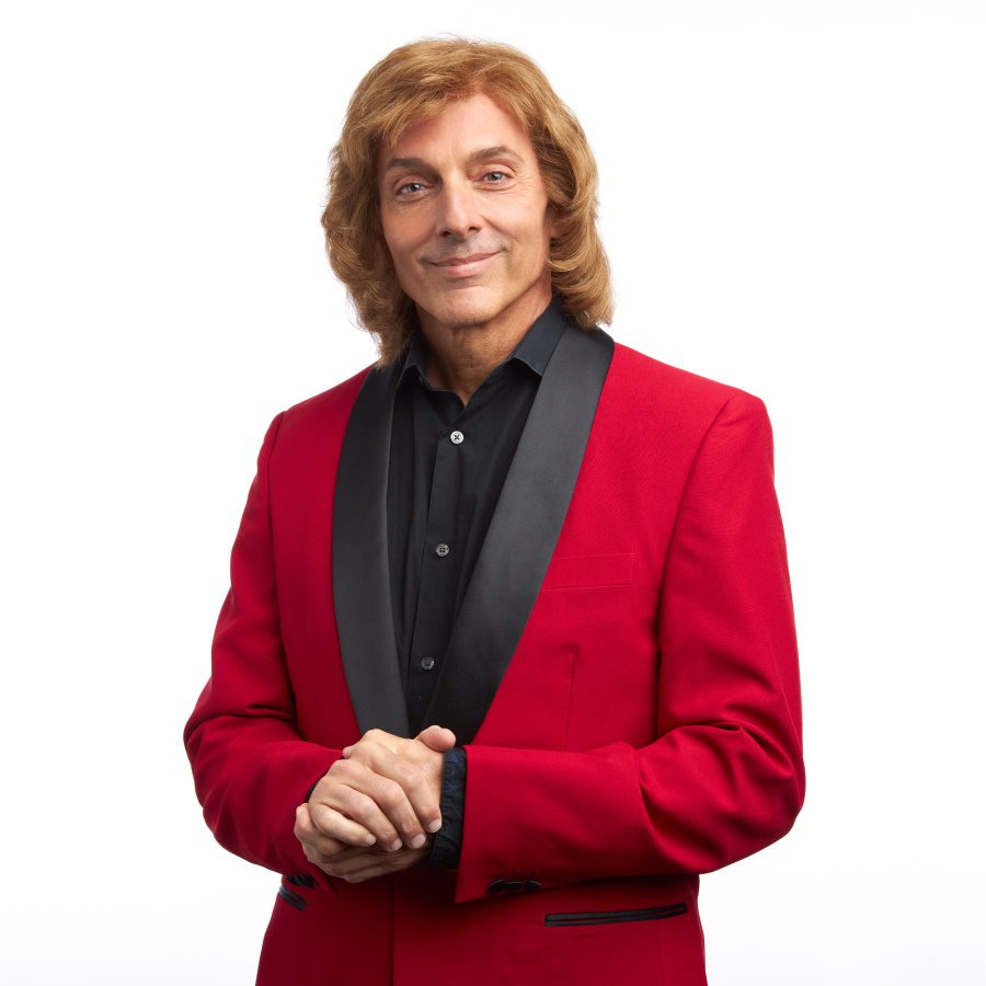 Barry Manilow tribute artist Joe Hite, wearing a red jacket and black shirt and a custom made Barry Manilow wig