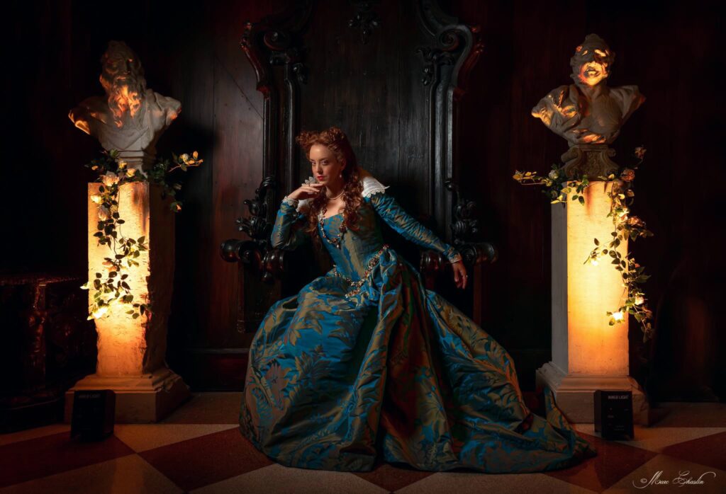 portrait of a woman in a blue and gold gown seated against a dark wall